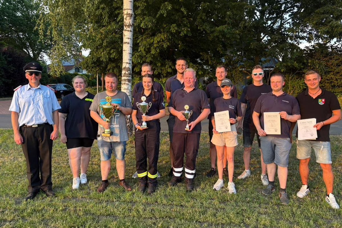 Group of twelve people standing on grass outdoors, posing with trophies and certificates after a competition or event.