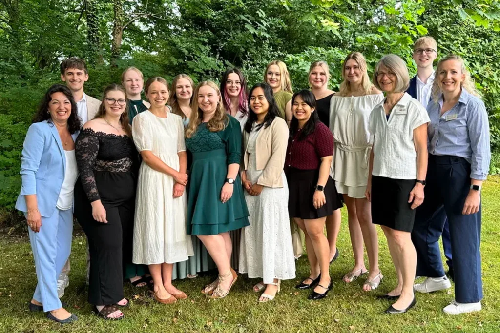 Group of young adults and two older women posing outdoors in a garden, dressed in semi-formal attire.