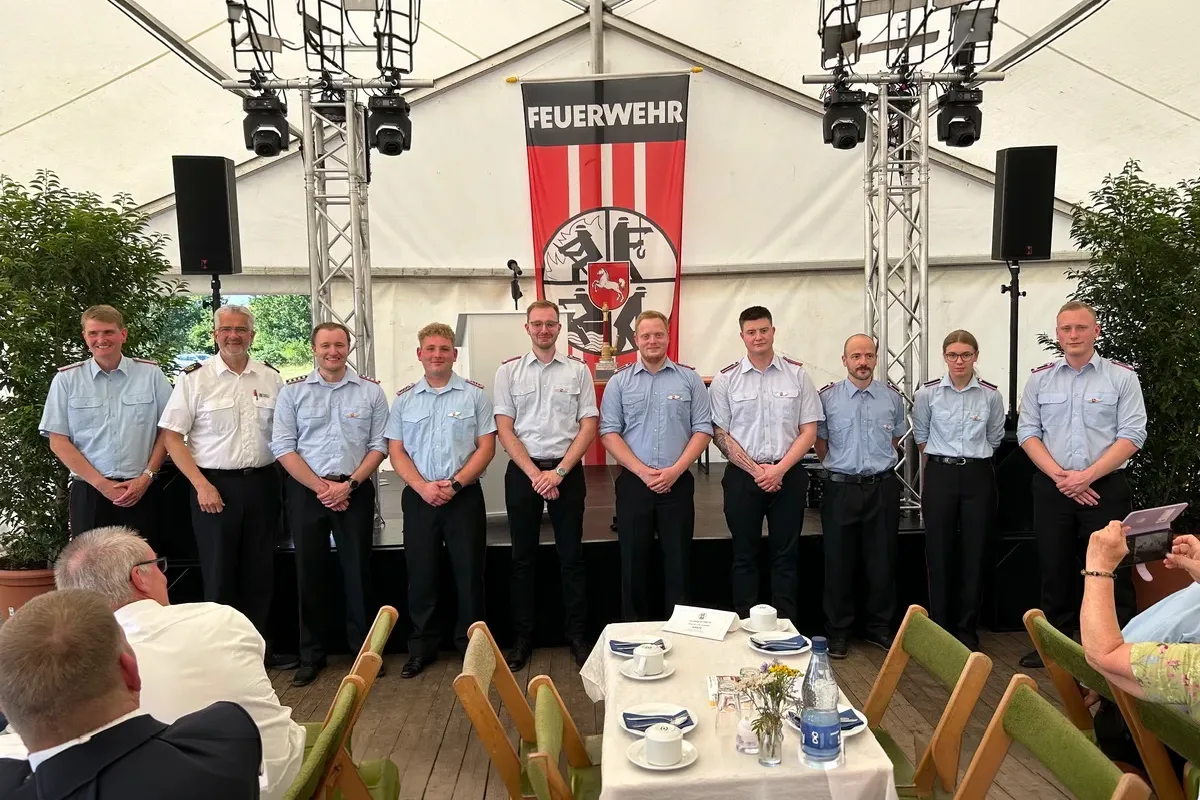 Group of firefighters in light-blue shirts posing on stage in front of a Feuerwehr banner during an event.