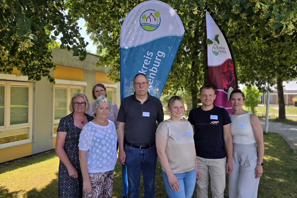 Group of six adults posing outdoors at a community event with two tall banners in the background.