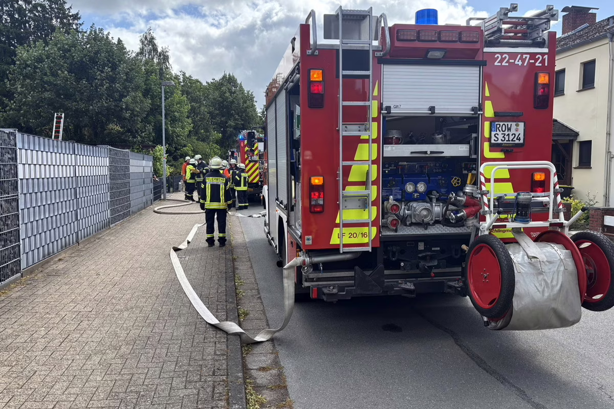 Firefighters in high-visibility gear and helmets lay out a hose beside a red fire engine on a residential street, coordinating the response.