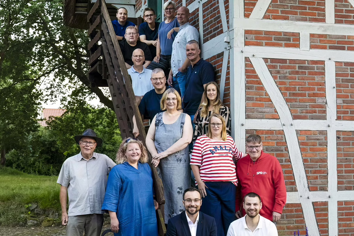 Group of coworkers posing on an outdoor wooden staircase beside a red brick timber-framed building, smiling at the camera.