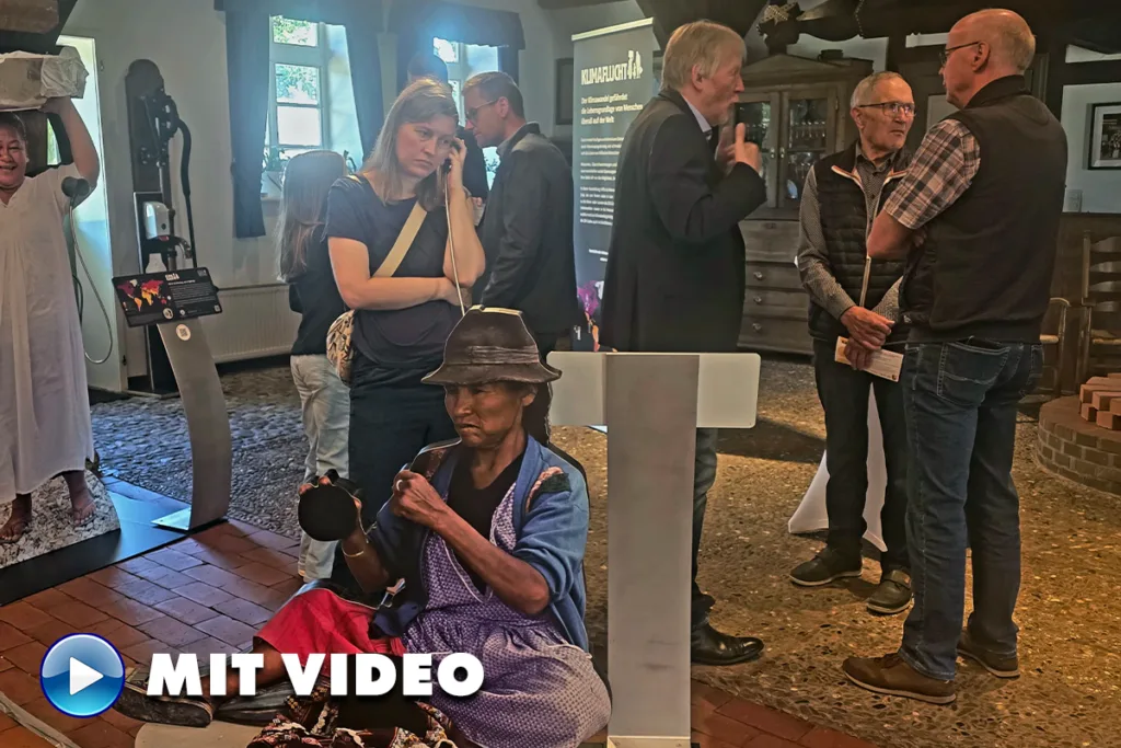 Museum scene with visitors conversing; a woman on a phone in the foreground and a lifelike seated statue wearing a hat nearby.