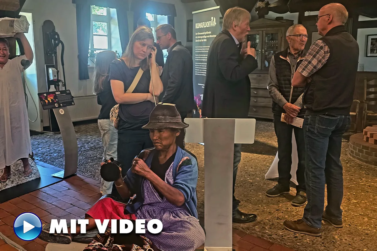 Museum scene with visitors conversing; a woman on a phone in the foreground and a lifelike seated statue wearing a hat nearby.