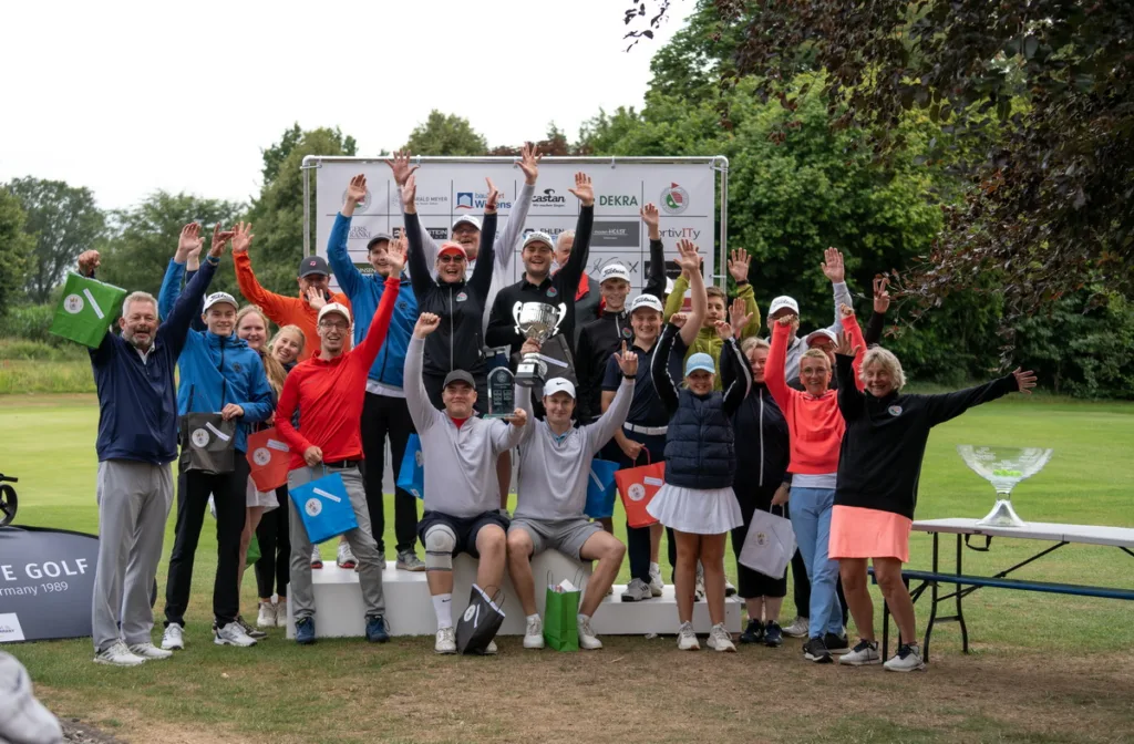 Group of golfers and supporters on a podium raising hands in celebration with a trophy at an outdoor awards ceremony on a golf course.