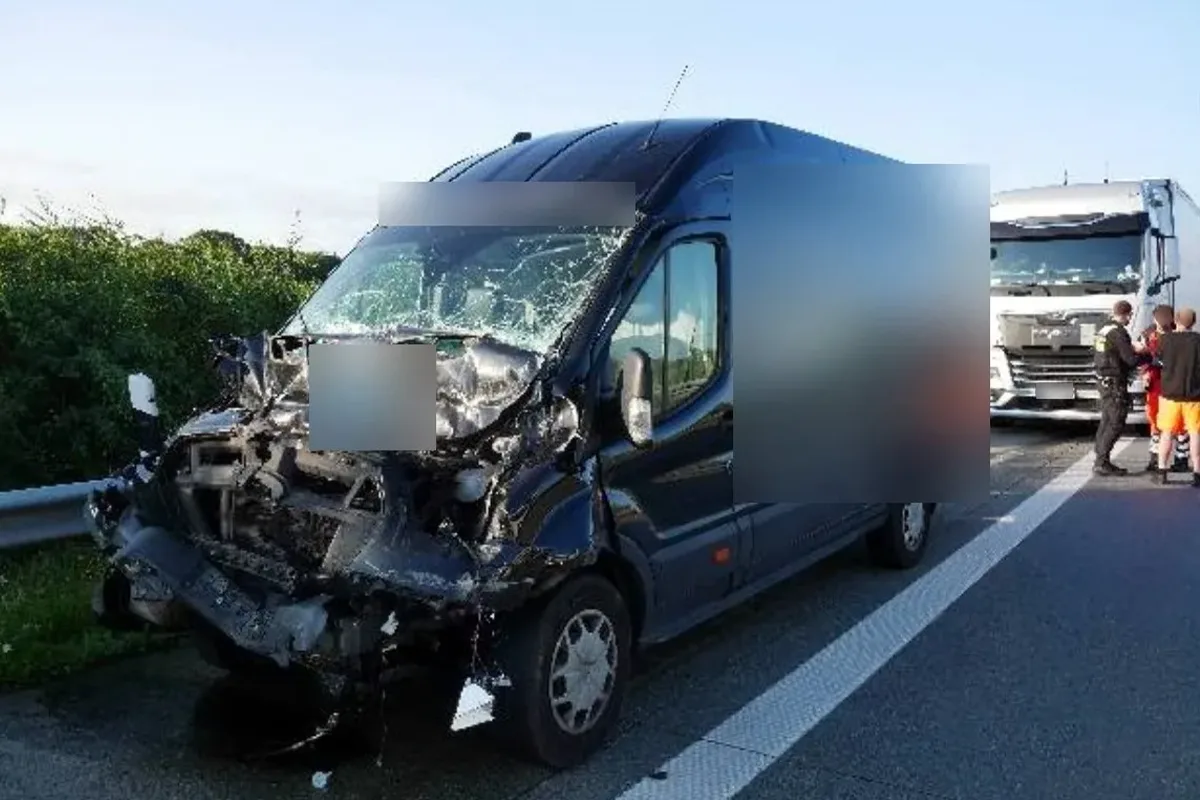 Blue van with severe front-end damage after a highway crash; a large truck and bystanders are in the background.