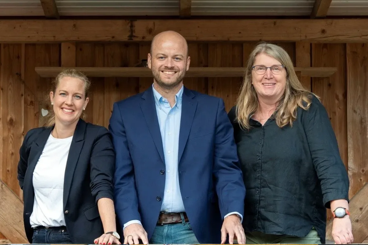 Three professionals pose together in front of a wooden backdrop, smiling at the camera.