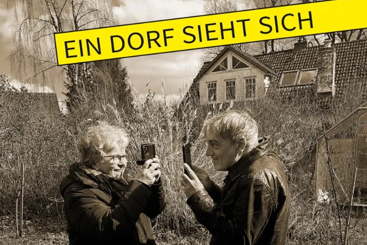 Zwei ältere Frauen machen Selfies mit ihren Handys im Garten, gelber Banner oben mit dem Text 'EIN DORF SIEHT SICH'
