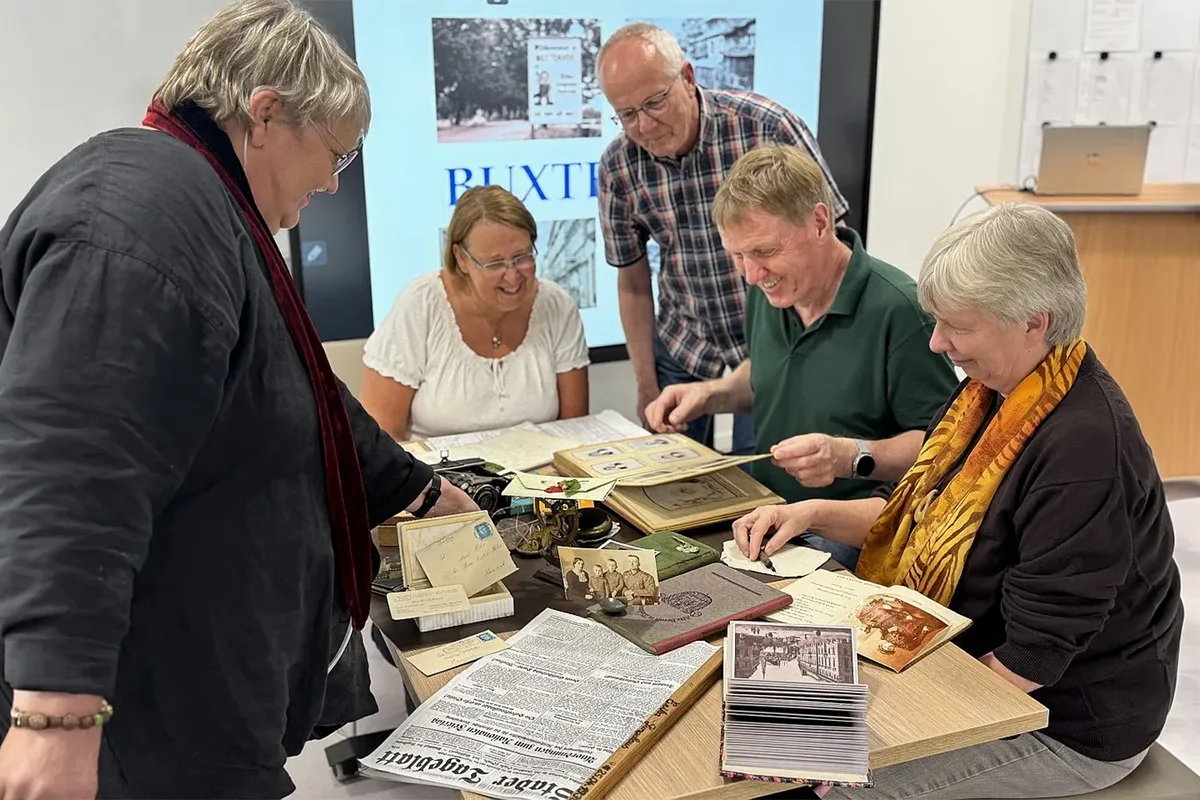 Five adults gather around a table, examining vintage photos, letters, and newspapers for a history project or archive activity.