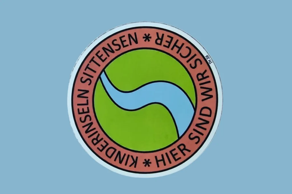 Circular sticker/patch: pink ring with black text around a green center featuring a blue curved shape.